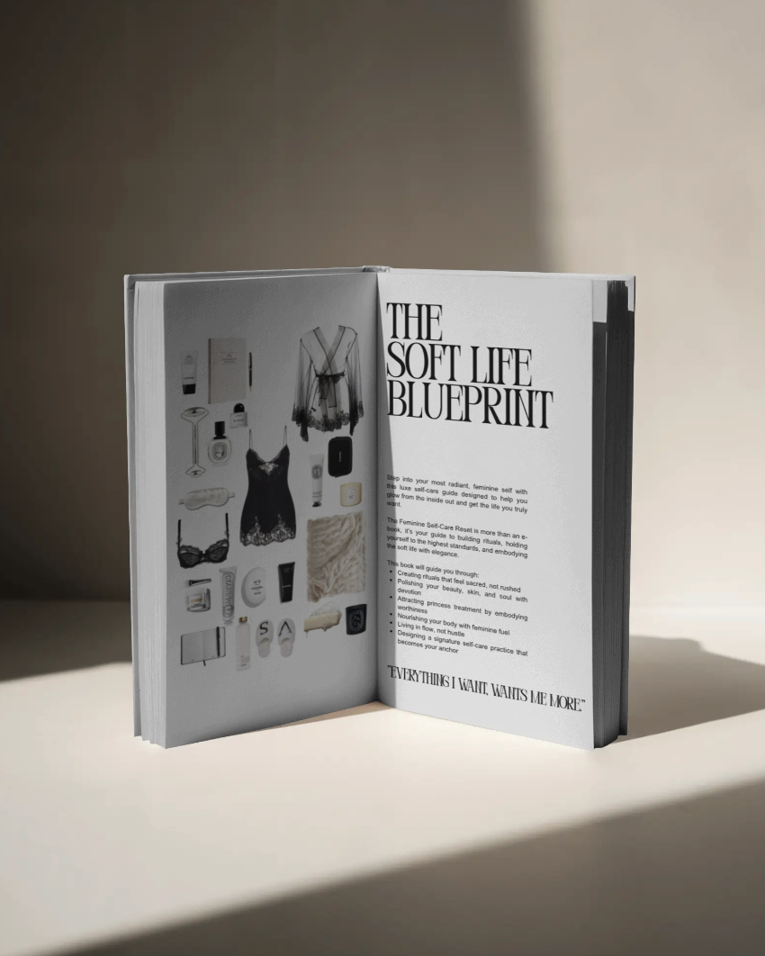 An open book titled "The Soft Life Blueprint" resting on a neutral beige surface, featuring a minimalist layout with luxury self-care items on one page and elegant typography on the other. The soft lighting and shadows evoke a quiet luxury aesthetic.
