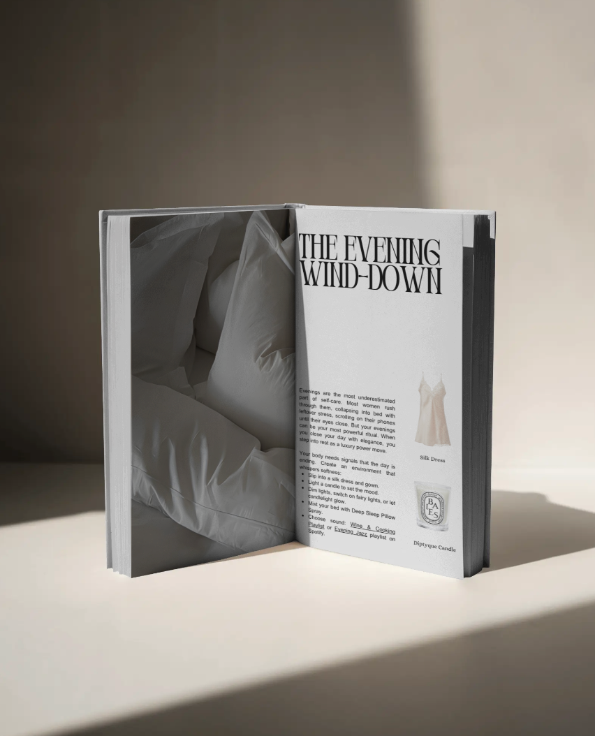 Open book on a neutral surface showing a page titled “The Evening Wind-Down”, featuring soft white bedding imagery and text about evening self-care rituals, including a silk dress and Diptyque candle.